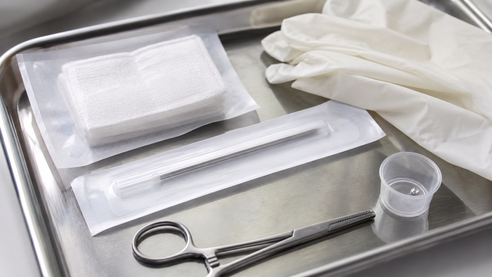 Sealed single-use piercing needle with sterile gauze, forceps, gloves, and starter jewelry