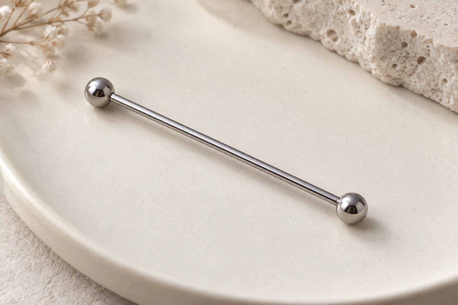 A long straight silver-colored barbell with two round ends on an ivory surface.