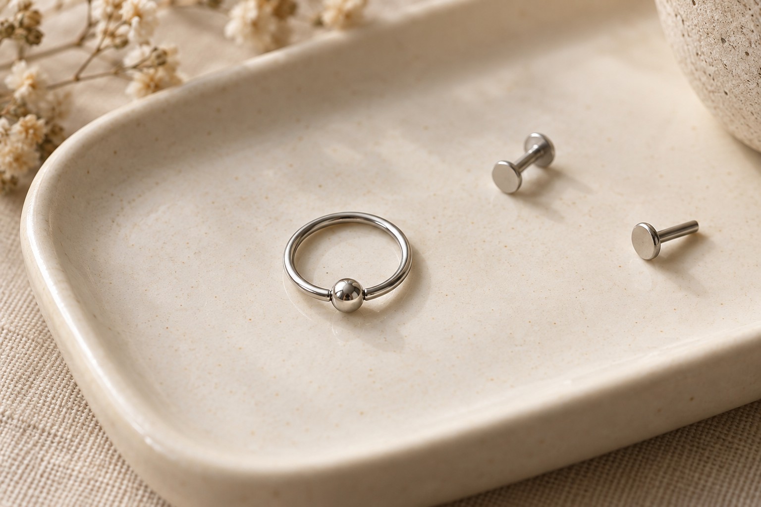 A silver-colored bead ring and two separate flat-back studs on an ivory tray.