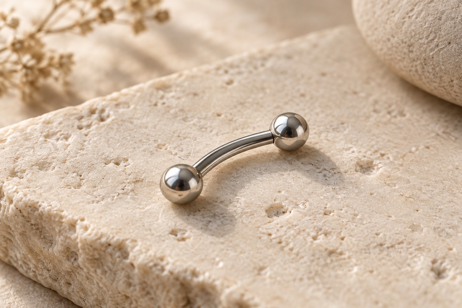 A short silver-colored curved barbell with a ball at each end on pale stone.