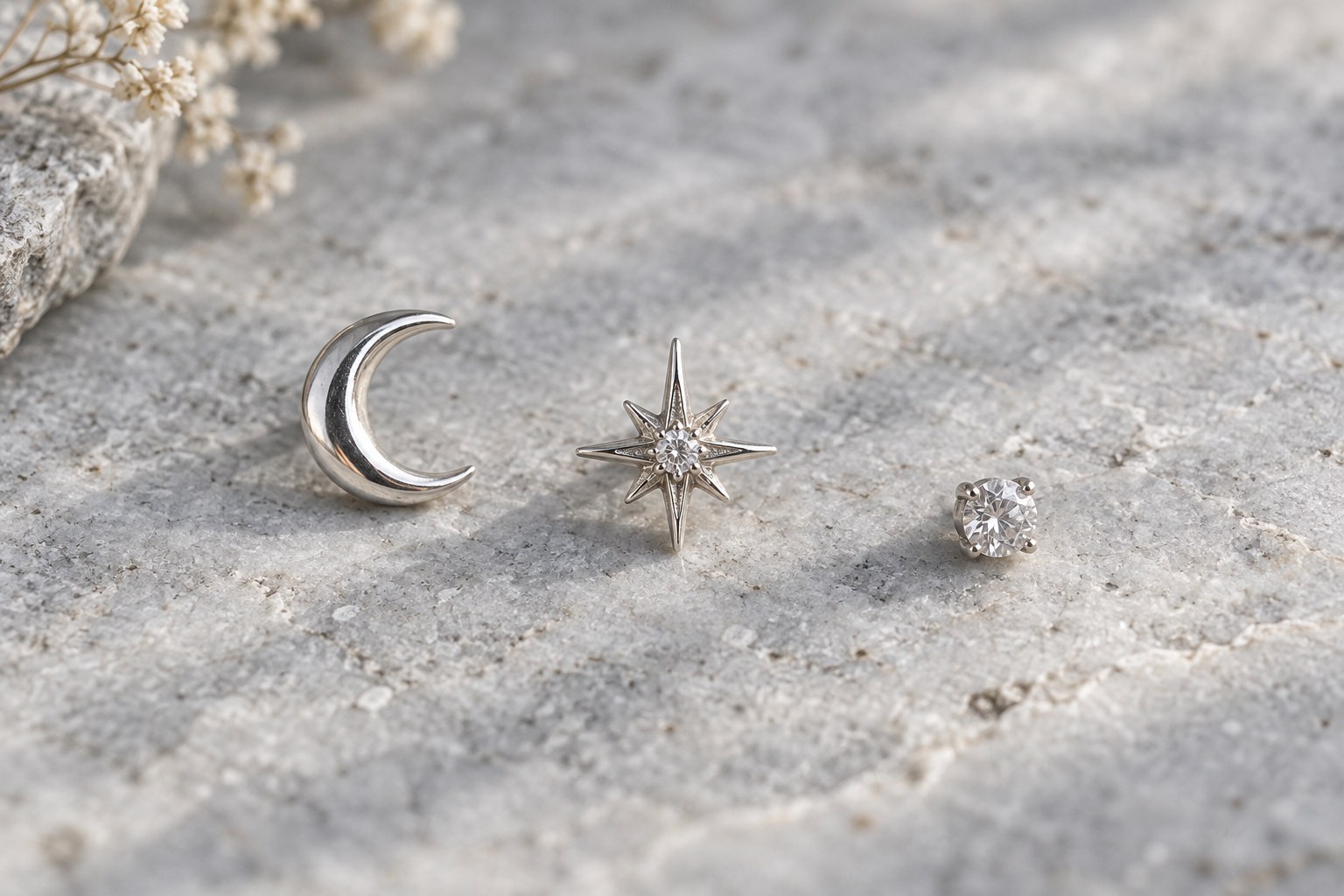 A crescent moon, pointed star and small crystal stud arranged separately.