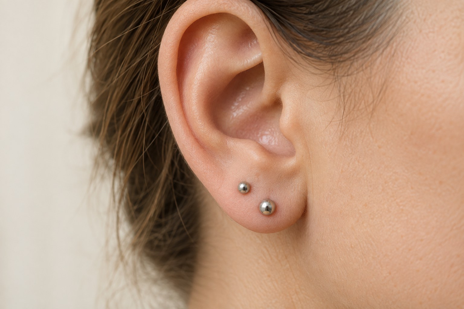 Two small silver-tone studs worn one above the other on an adult earlobe.