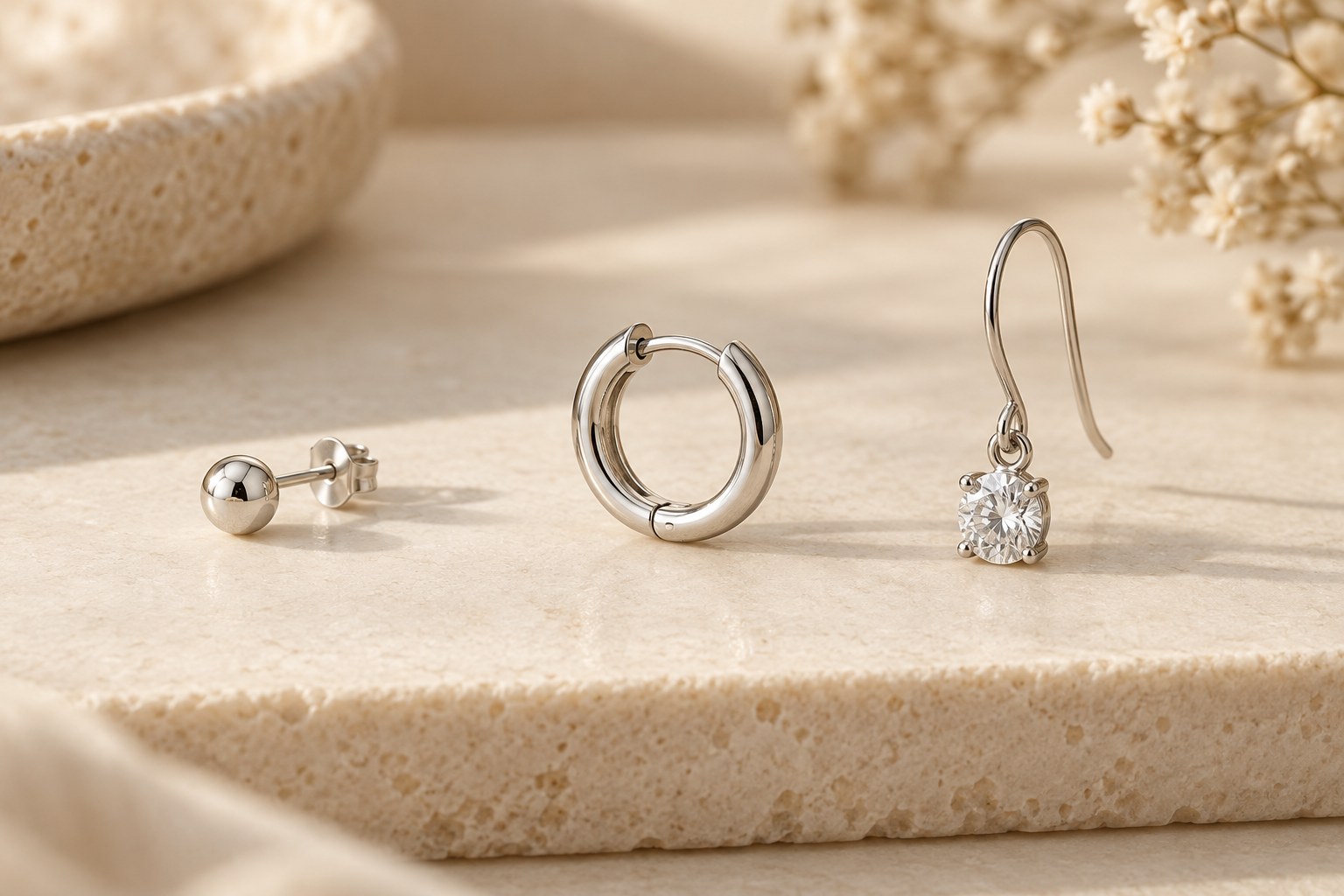 A round stud, small hoop and crystal drop earring arranged on a cream surface.