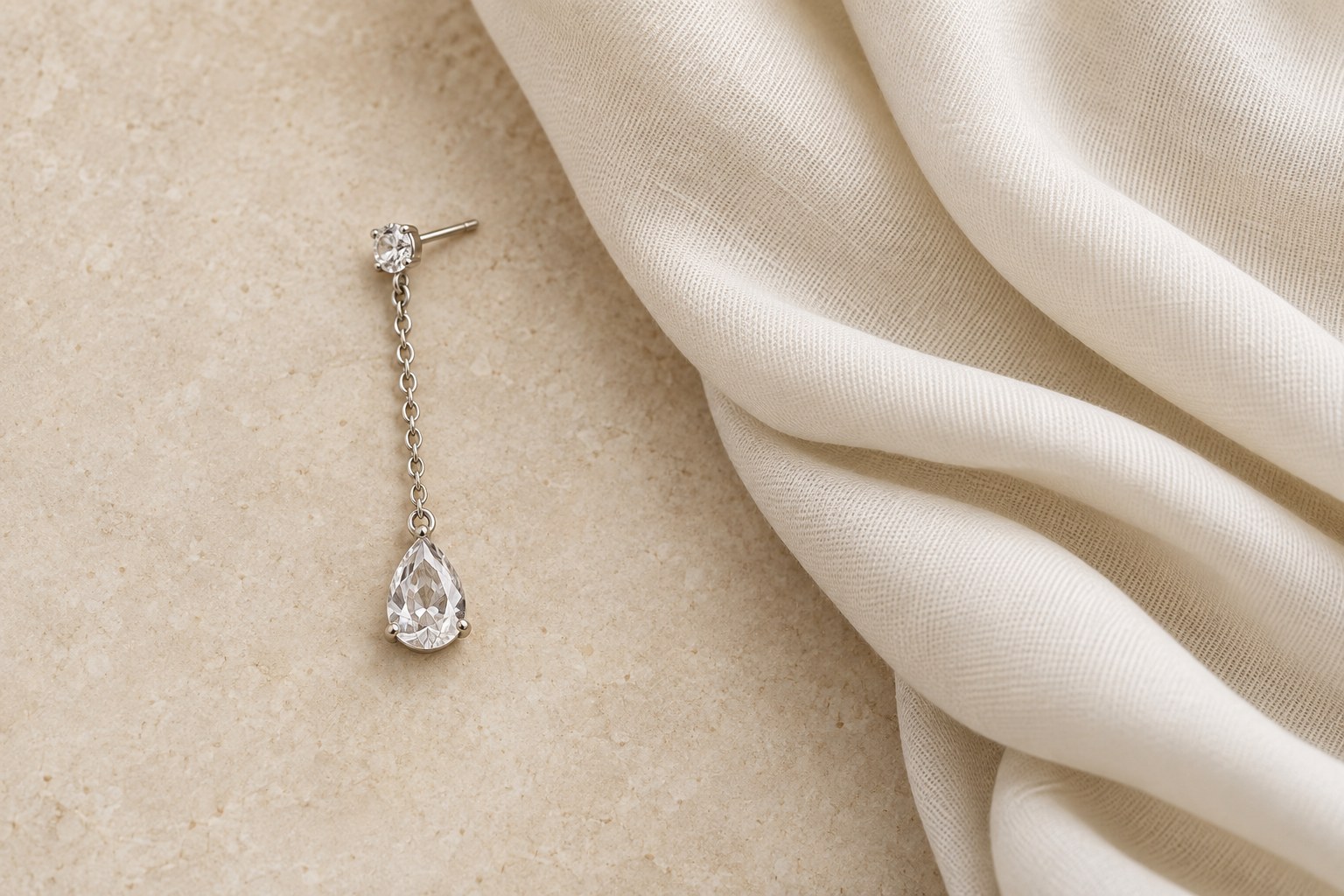 A crystal drop earring laid beside a folded cream scarf.