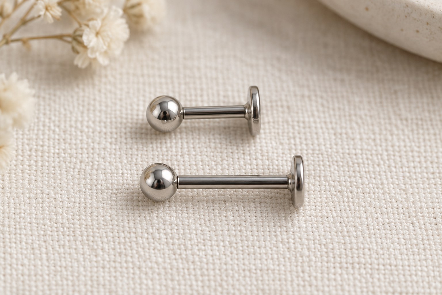 Two ball-front flat-back studs with different post lengths on pale fabric.