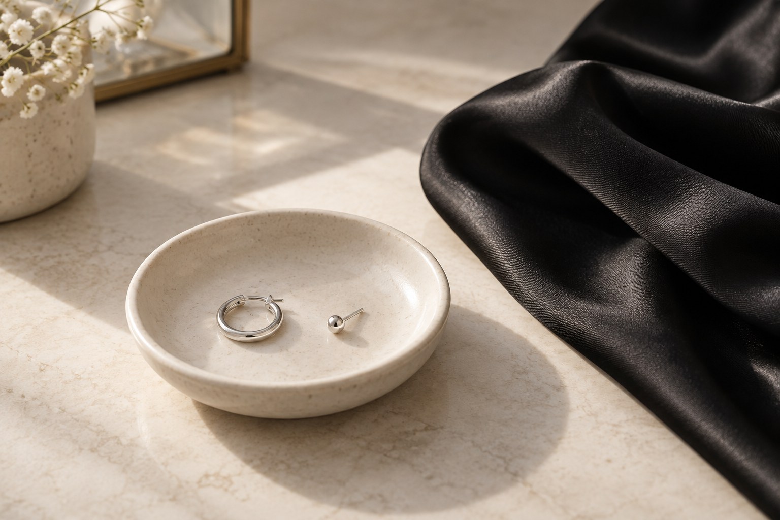 A hoop and a stud on a ceramic dish beside dark fabric.