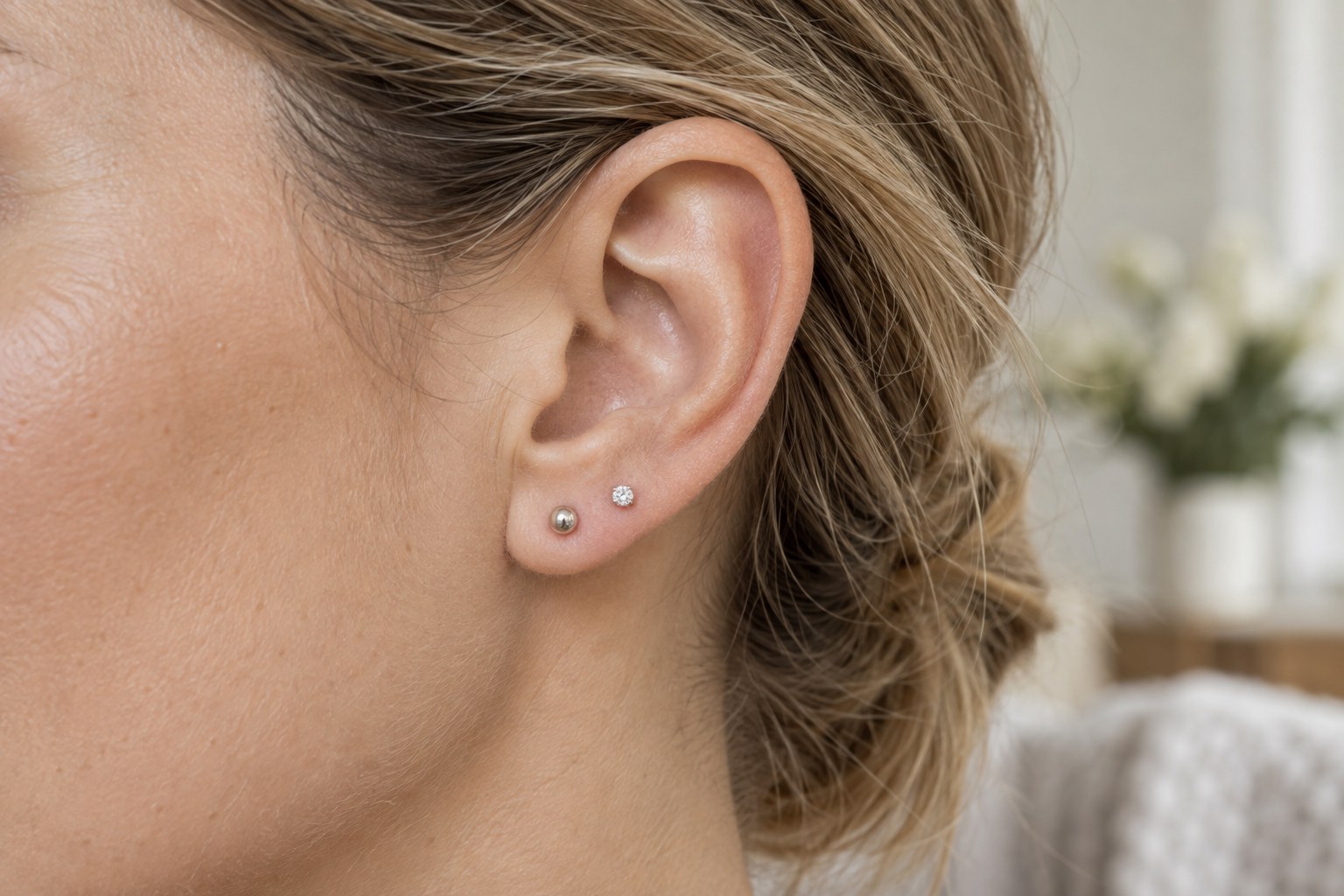 An adult earlobe wearing small round studs and a clear-stone stud.