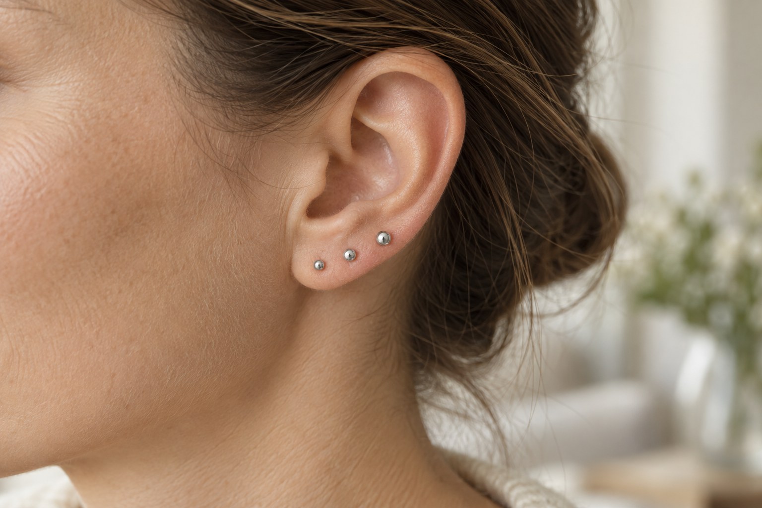 Three small ball studs following the curve of an adult earlobe.
