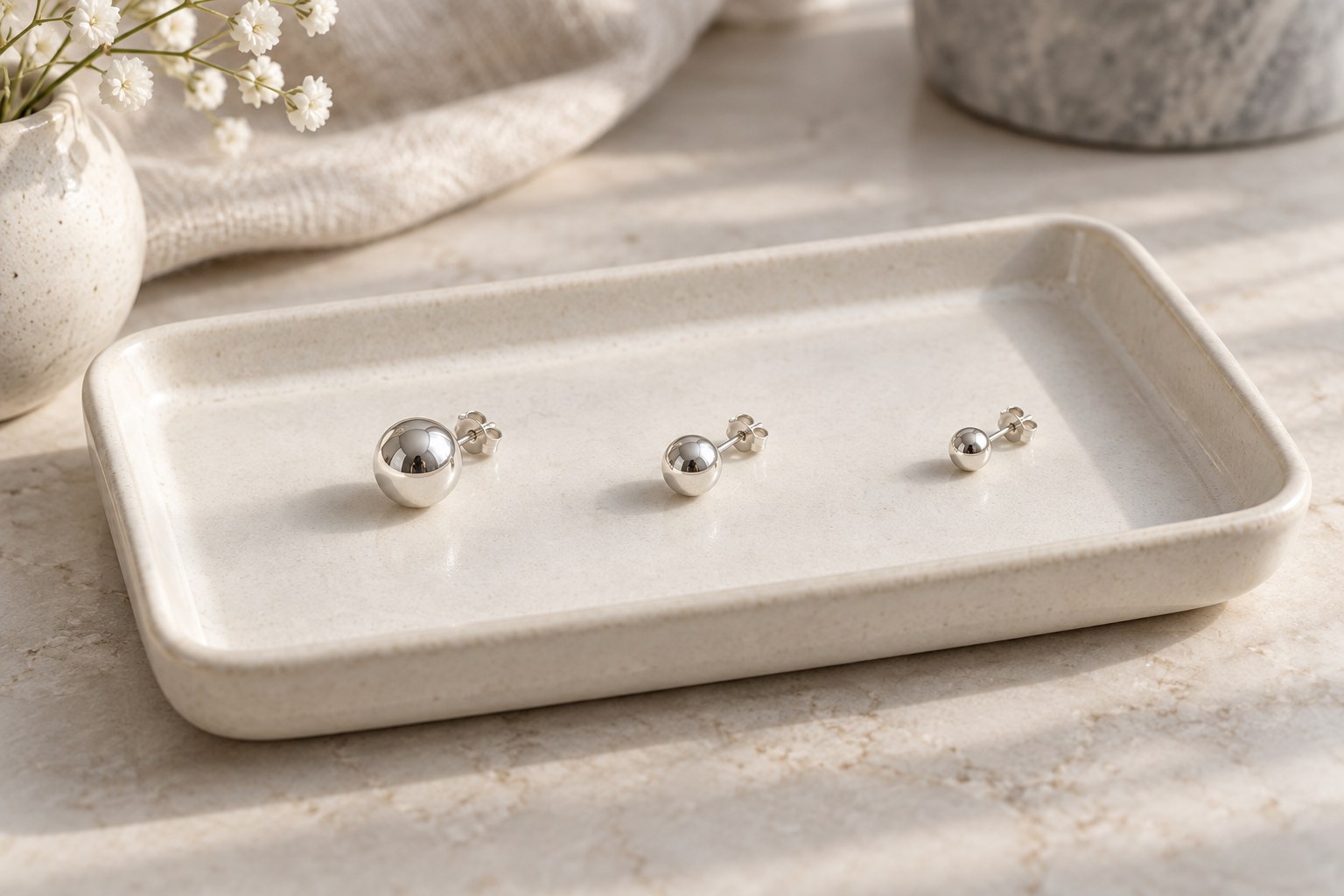 Three round ball studs in different sizes on a jewelry tray with butterfly backs.
