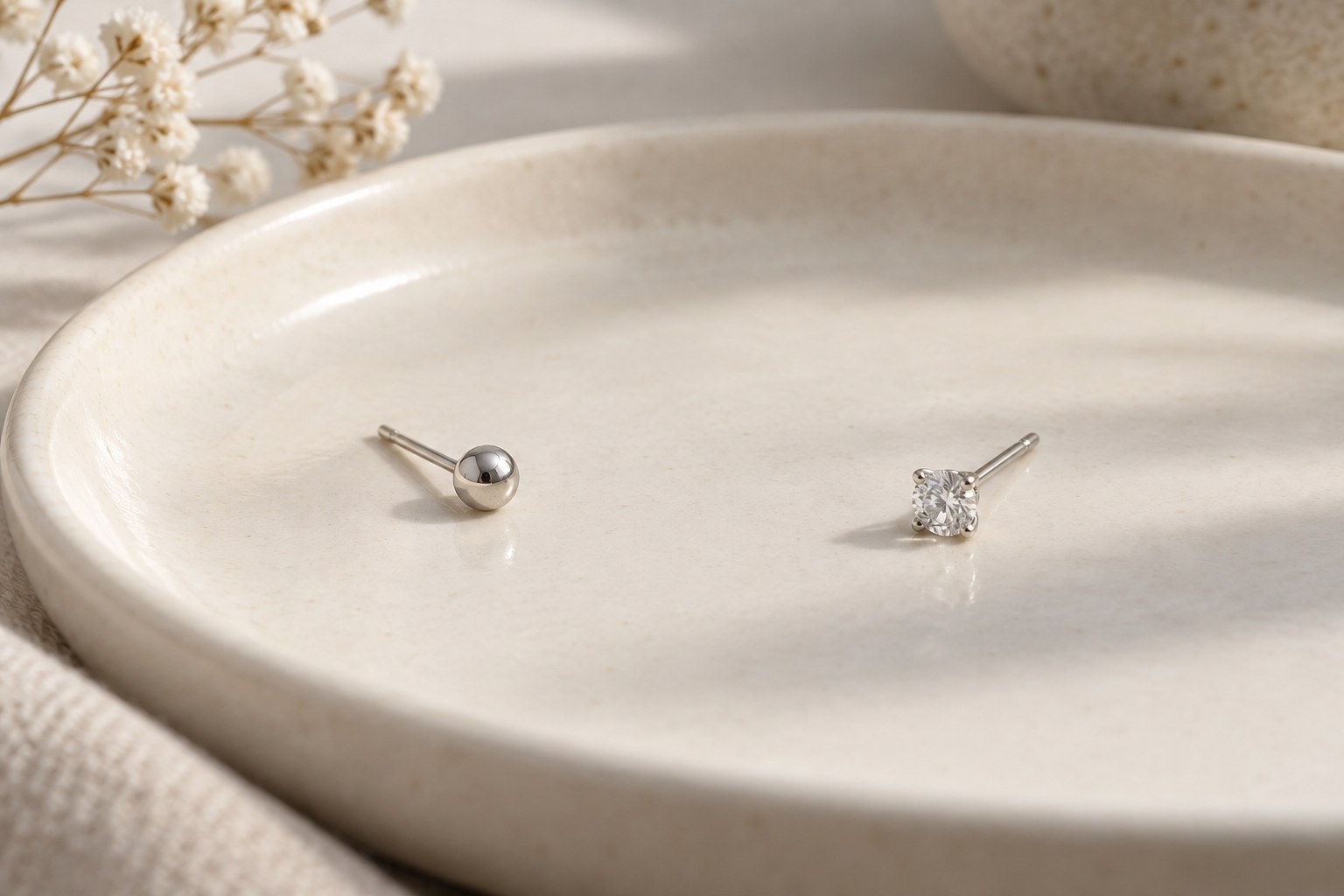 A round ball stud and a prong-set clear-stone stud on a plain surface.