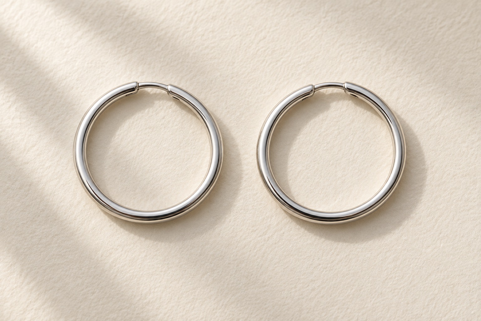 Two polished silver-tone circular hoop earrings on ivory paper.