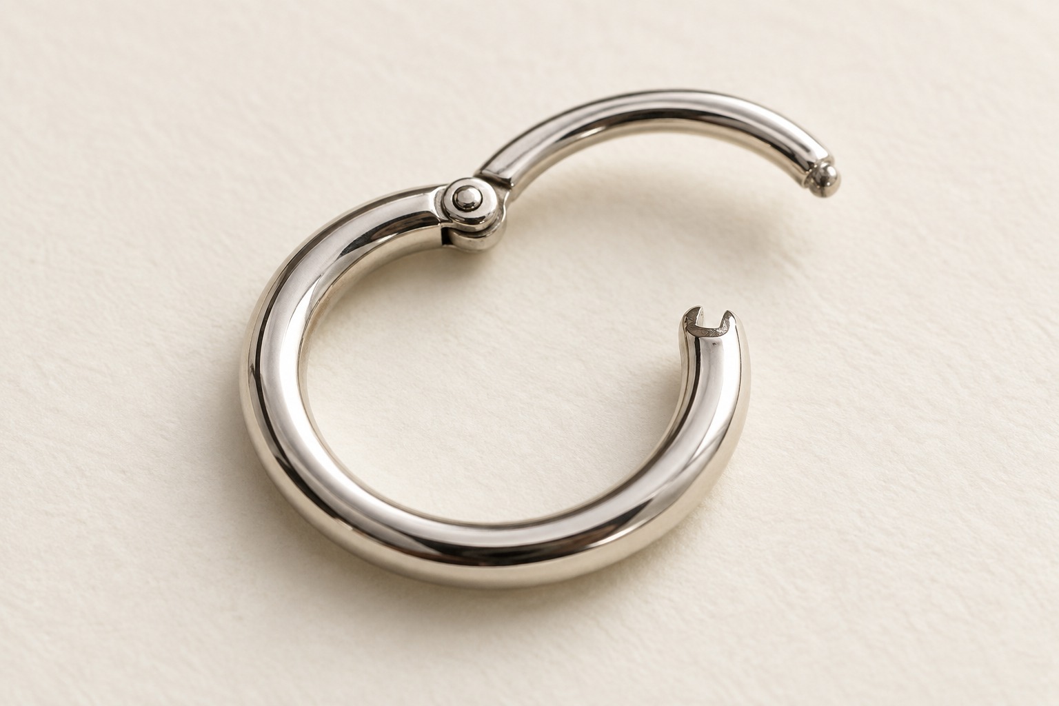 An open silver-tone hinged hoop on ivory paper.