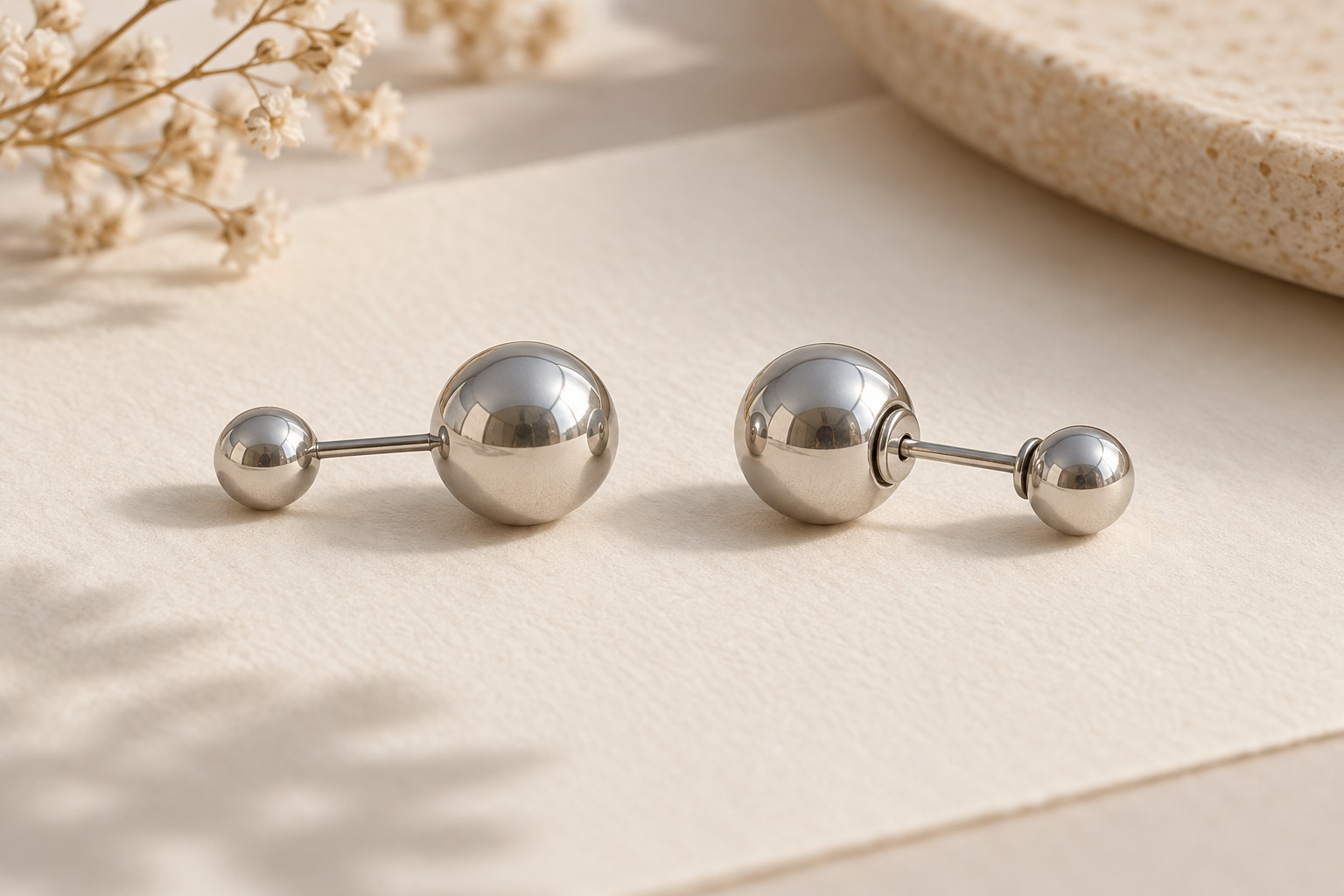 Two silver-tone double-ball earrings shown in profile on ivory paper.