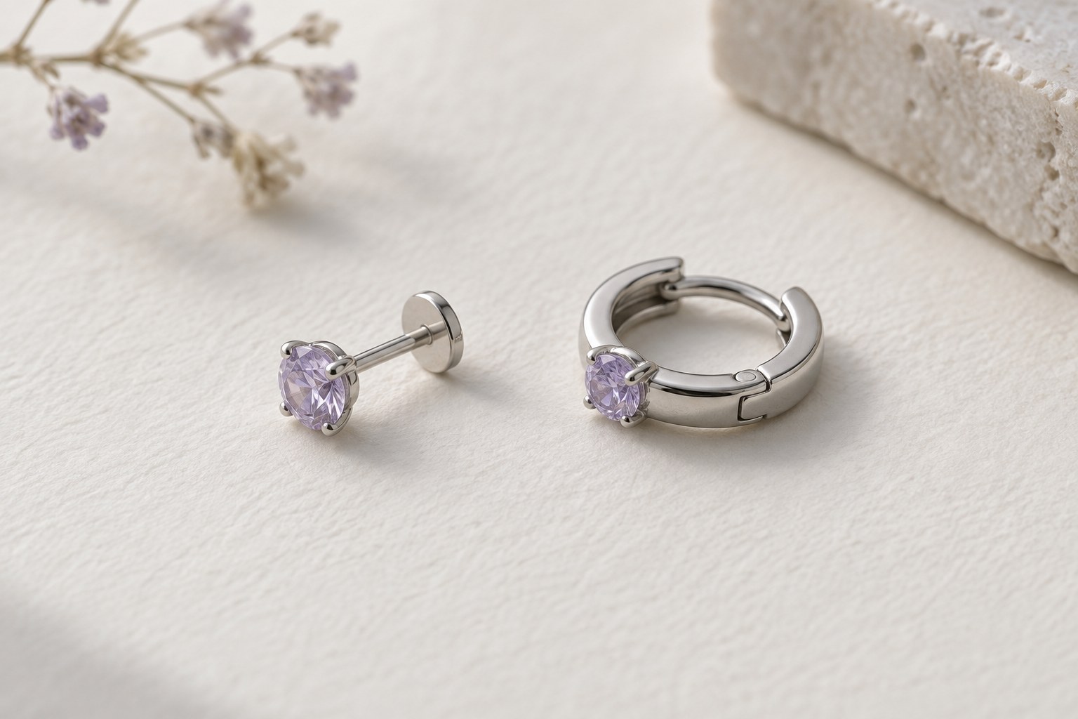 A lilac-colored flat-back stud beside a lilac-colored hinged hoop on ivory paper.