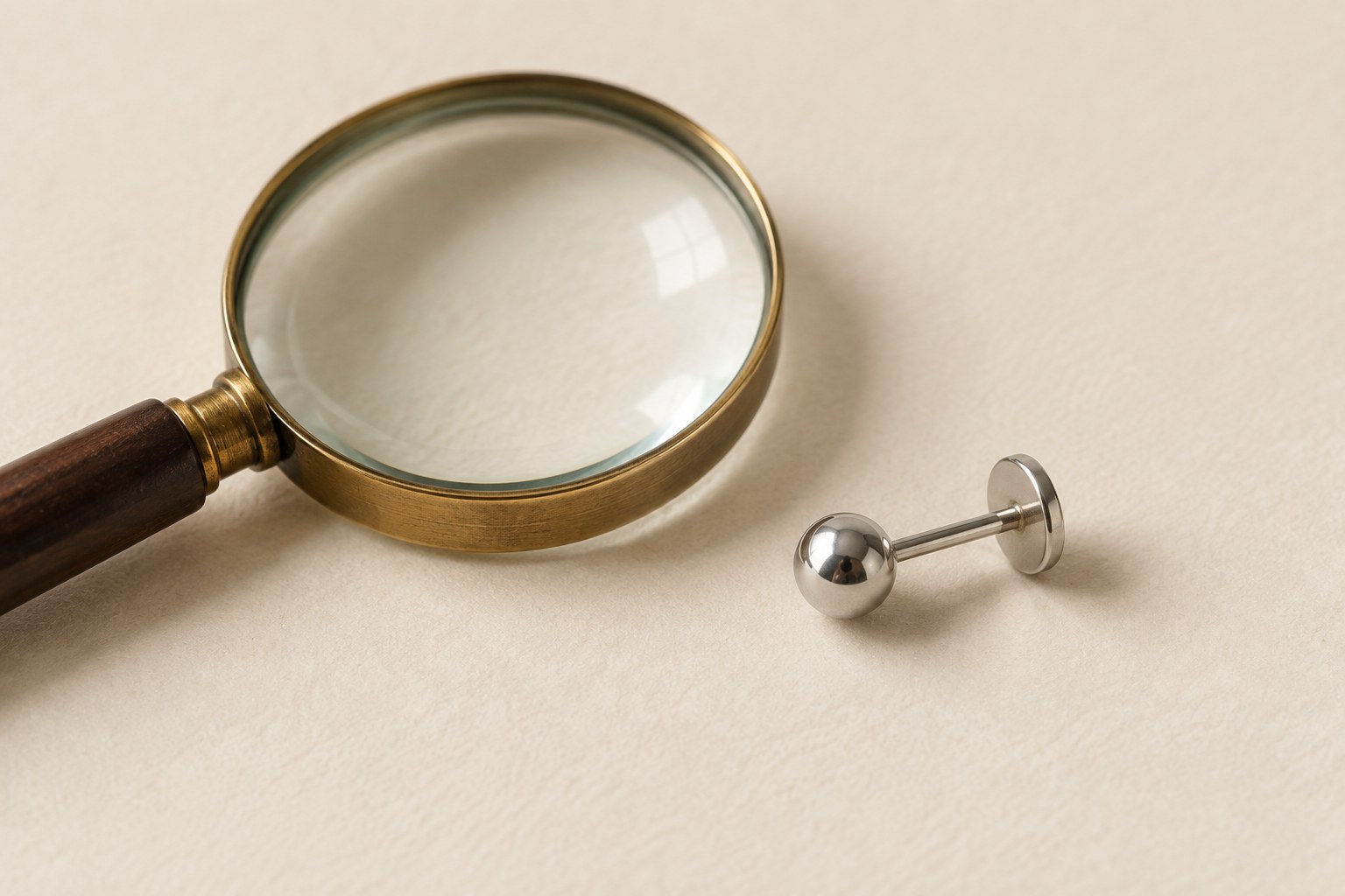 A magnifying glass beside a silver-tone ball stud with a straight post and flat rear disk.