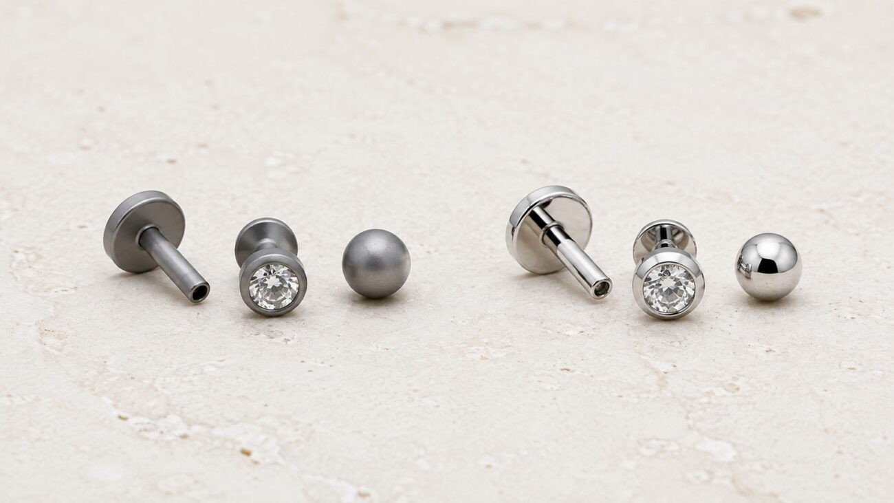 Titanium and surgical-steel earring samples arranged in two finish groups on pale stone