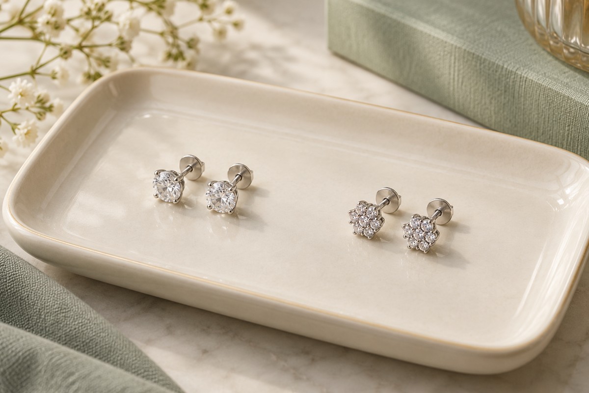 Two matching pairs of small silver-tone studs arranged separately on a cream tray.