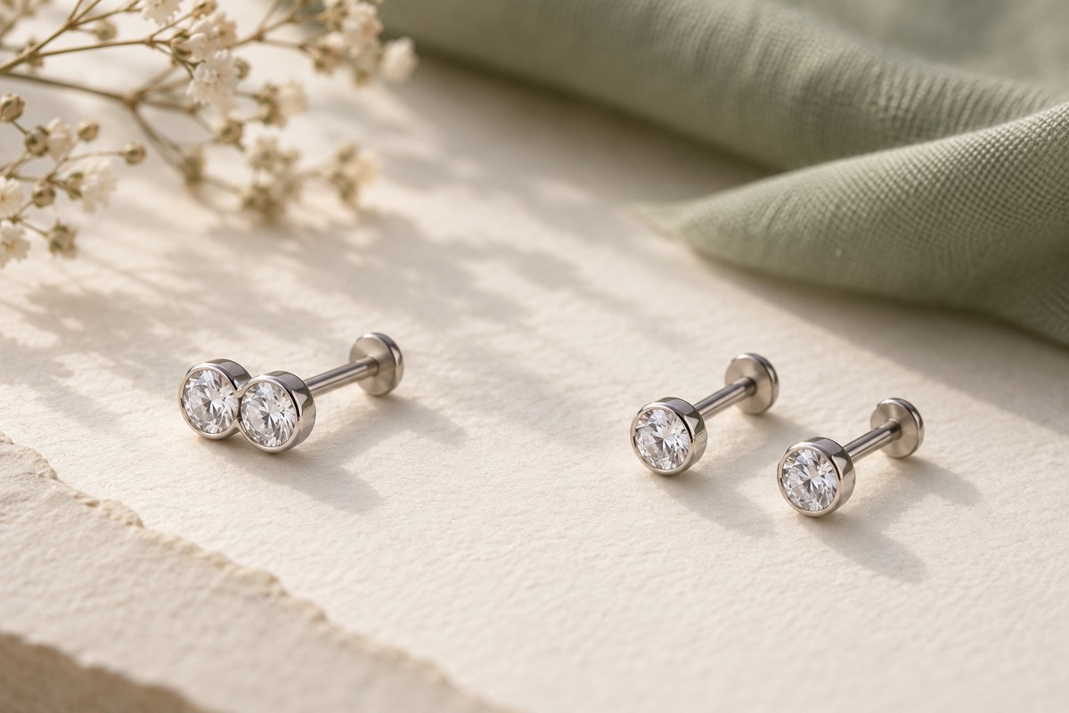 One silver-tone stud with a two-crystal front beside two separate round-front studs on cream paper.
