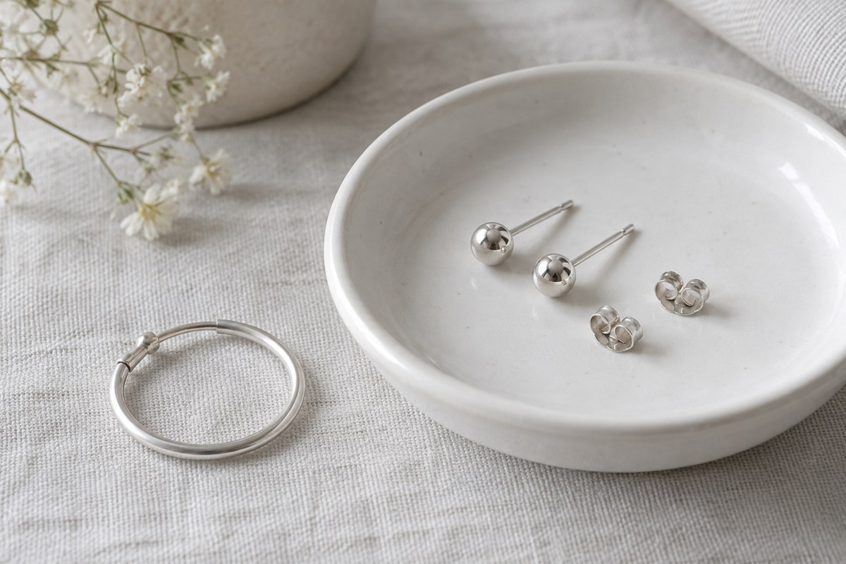 Silver-colored ball studs and butterfly backs on a dish beside a hoop.
