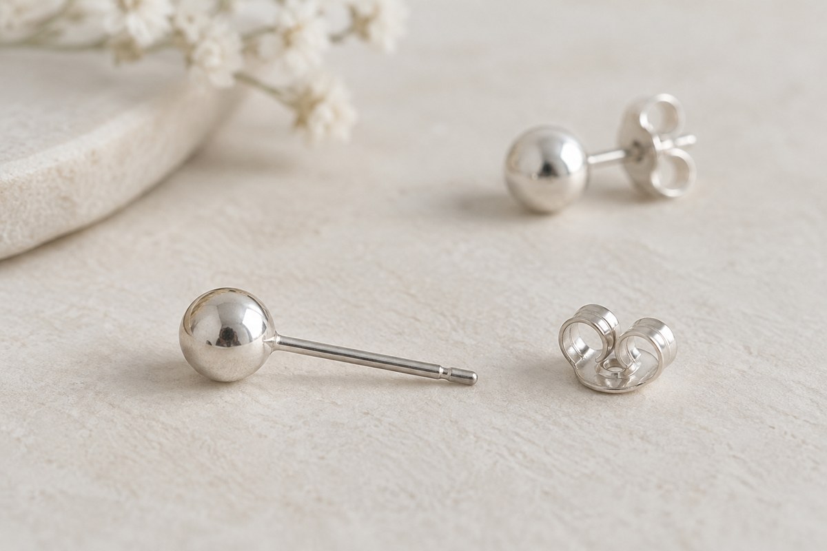A silver-colored ball stud and its separate butterfly back on an ivory surface.