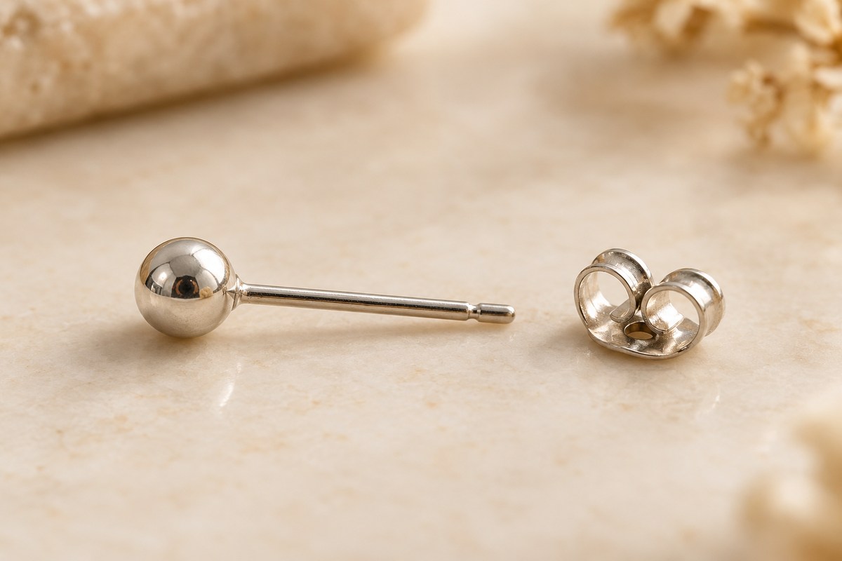 A silver-colored ball stud and its detached butterfly back on a cream surface.