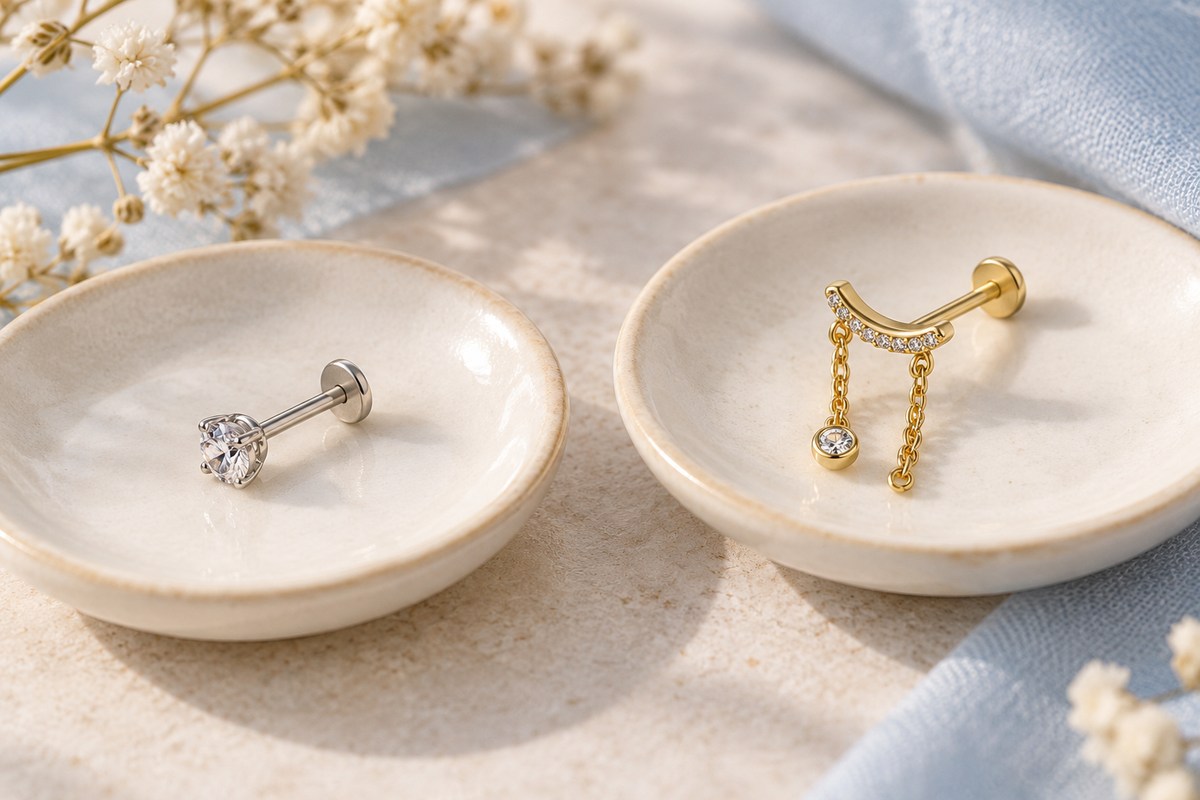 A straight crystal flat-back stud and a curved chain-drop earring on separate dishes.