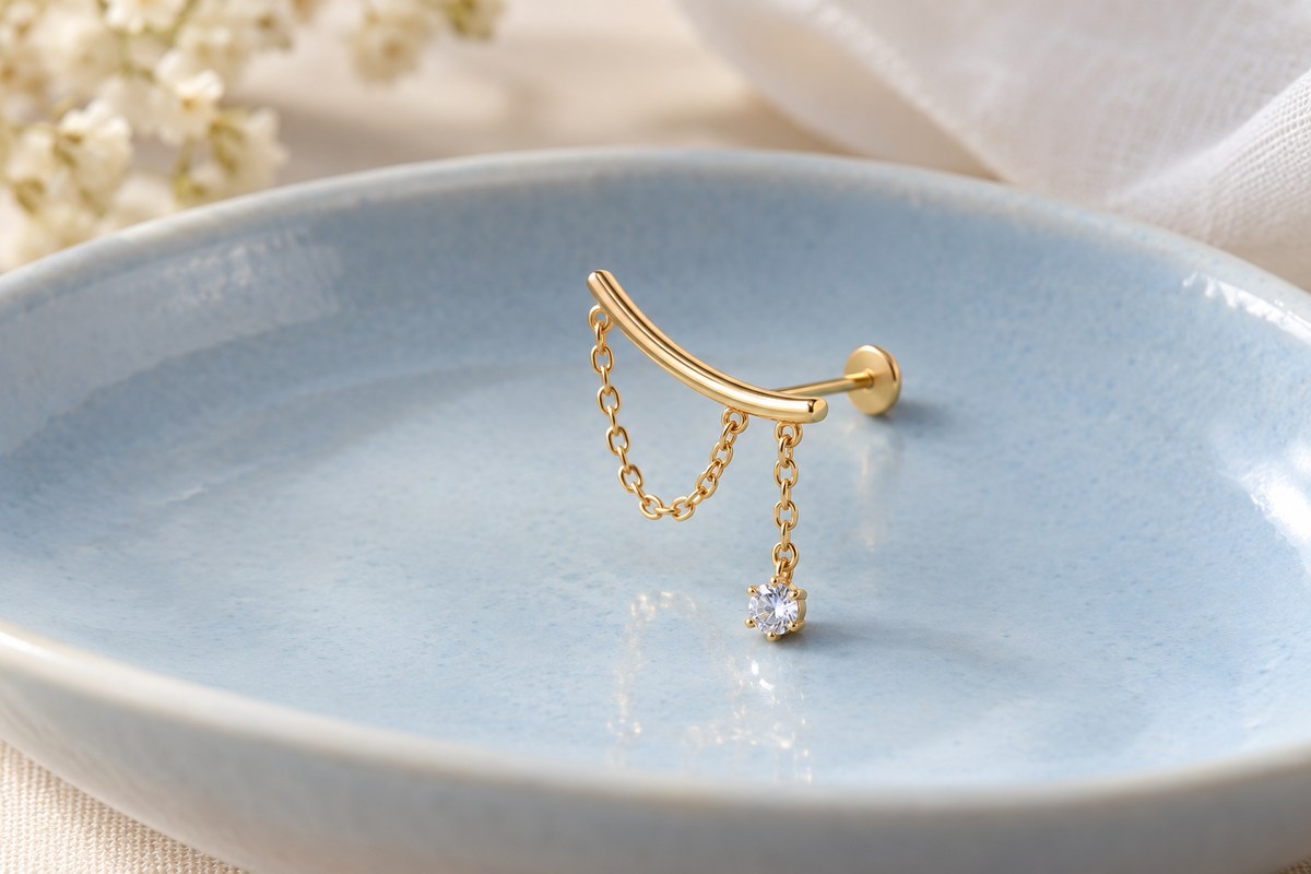 A curved gold-colored bar with a chain loop, crystal drop, post and flat disc on a blue dish.