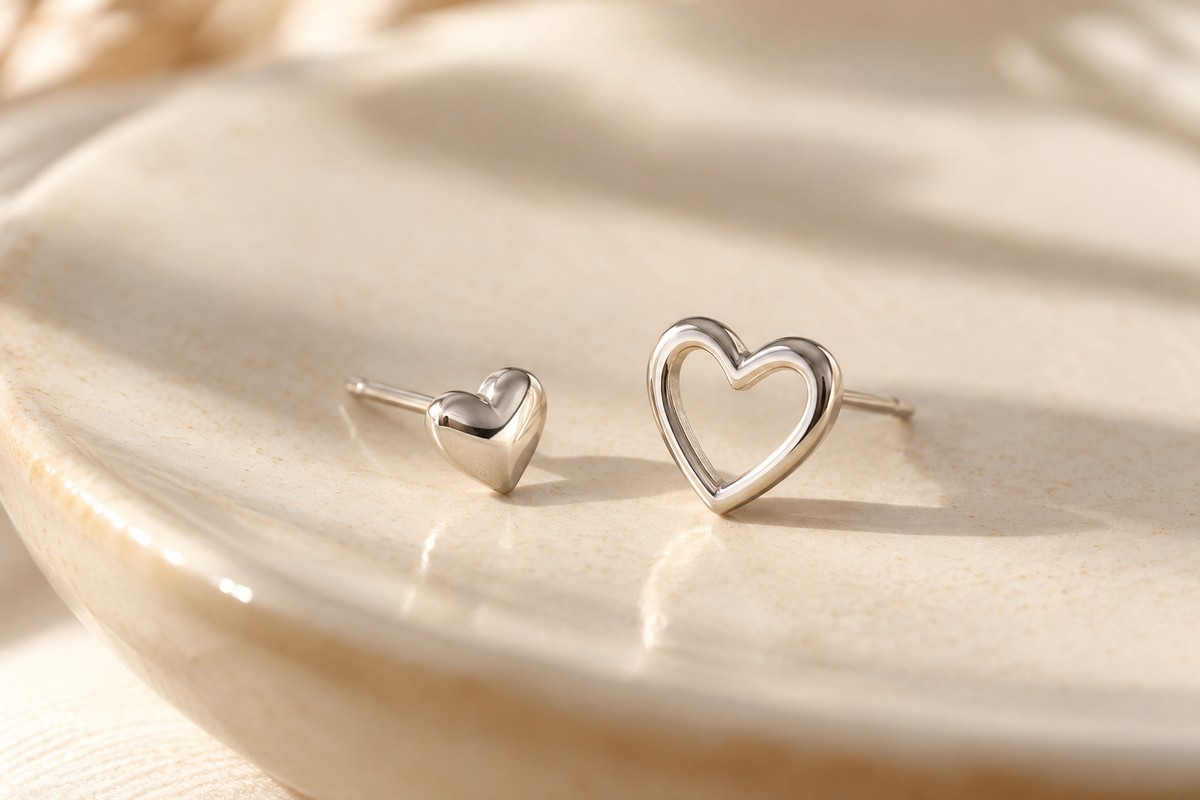 A polished filled heart stud beside an open-outline heart stud