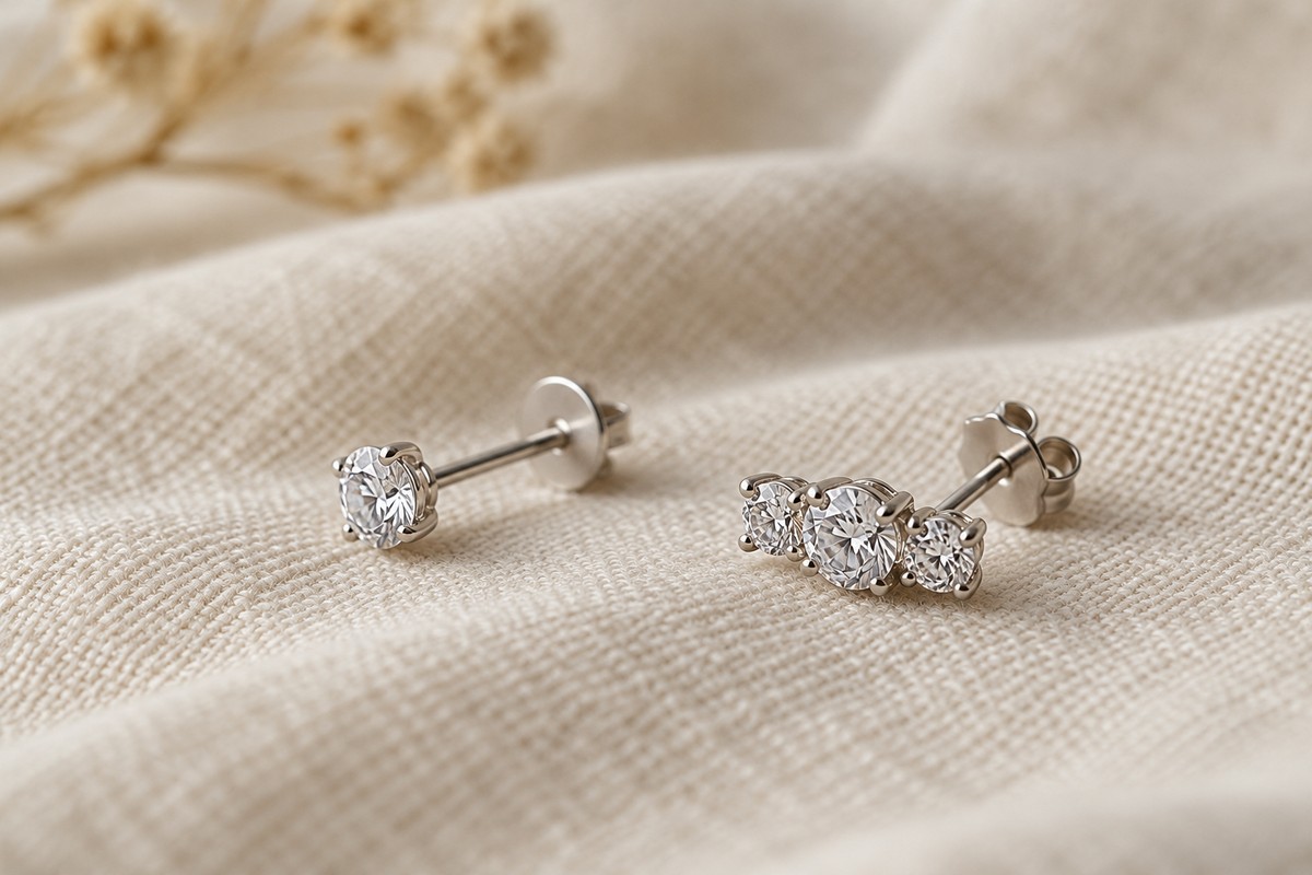 Side views of single-stone and three-stone studs on pale linen