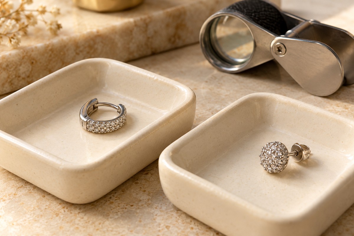 Small stone-set hoop and stud earrings on separate trays beside a loupe