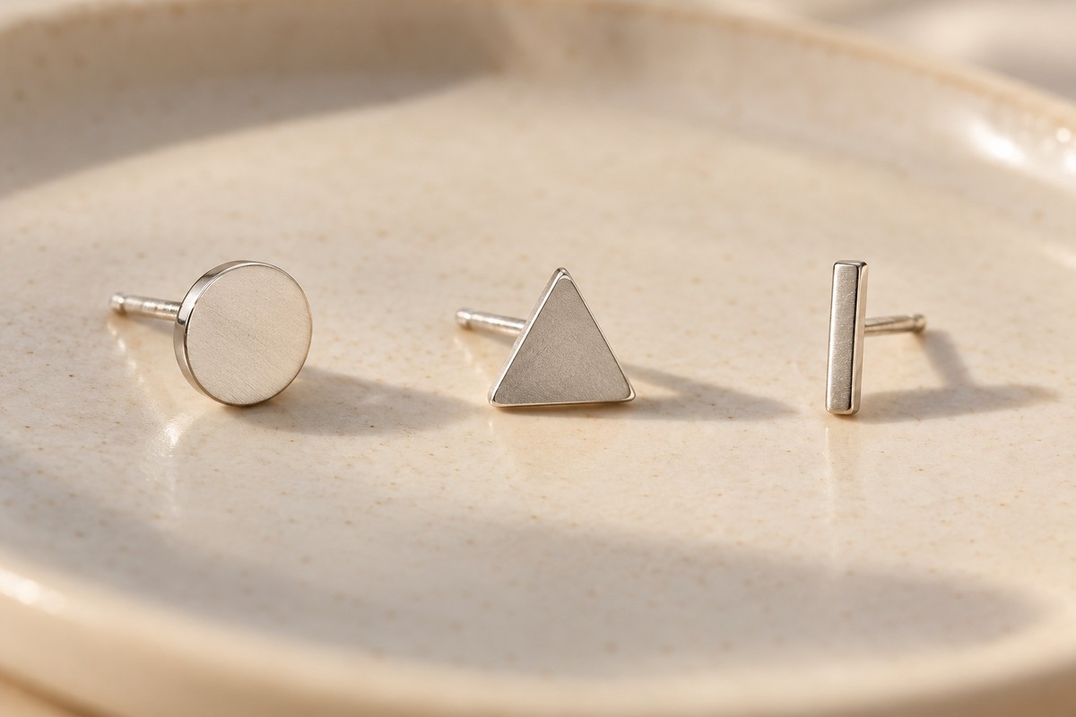 A flat circular stud, a triangular stud and a straight bar on cream ceramic
