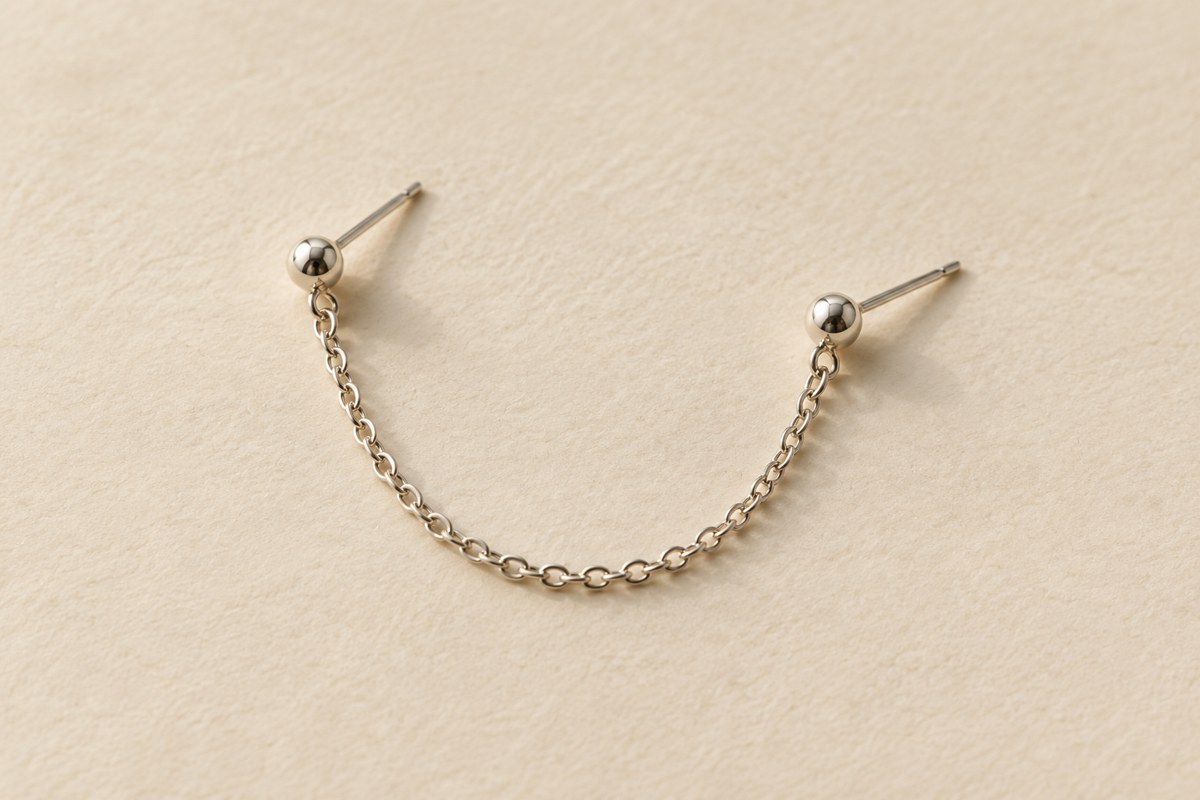 A silver-colored connector chain draped between two separate ball studs on a cream surface.