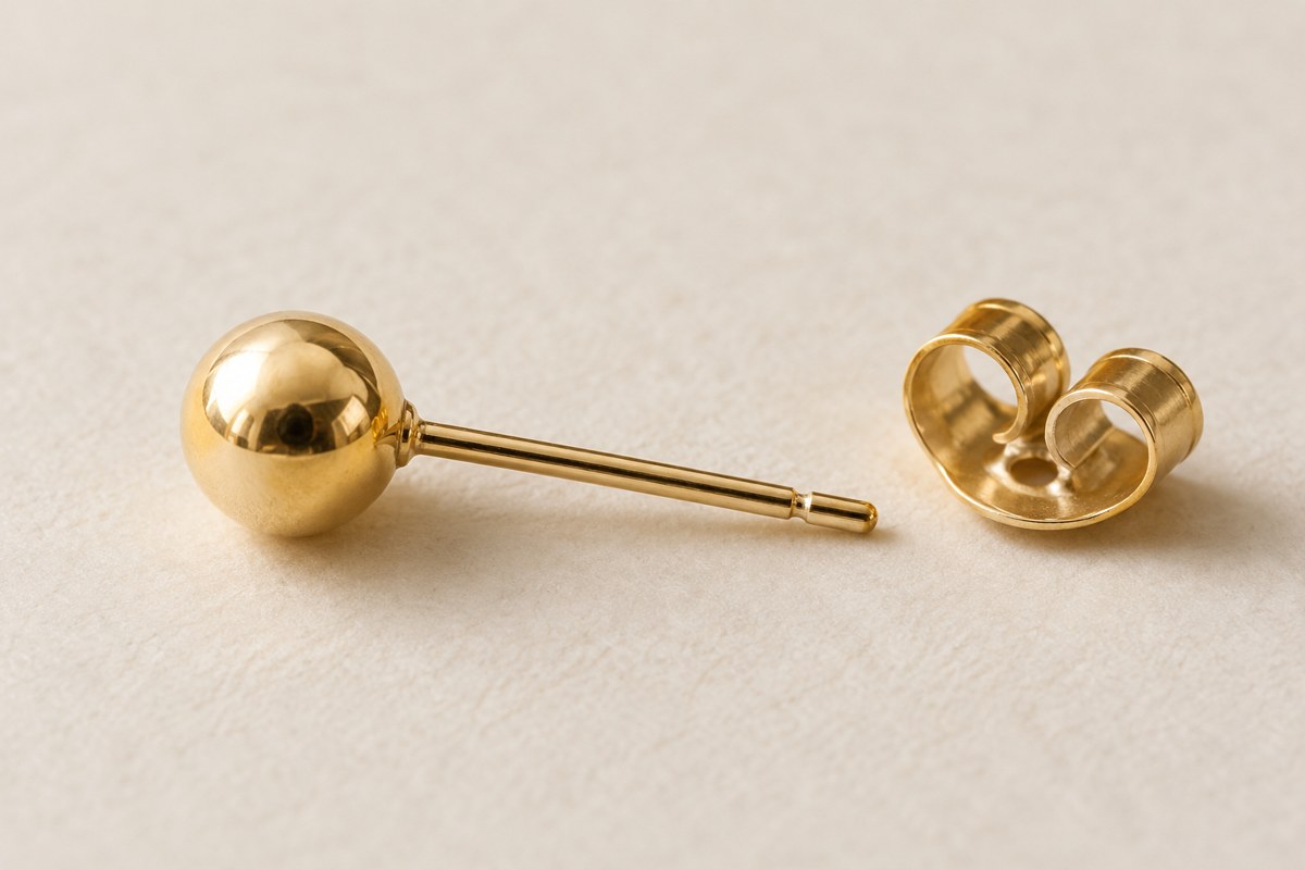 A gold-colored ball stud with a separate butterfly back on a cream surface.