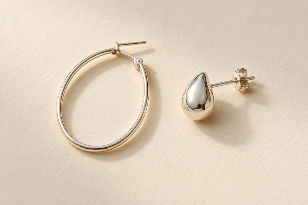 A silver-colored hoop beside a compact teardrop stud on a cream surface.