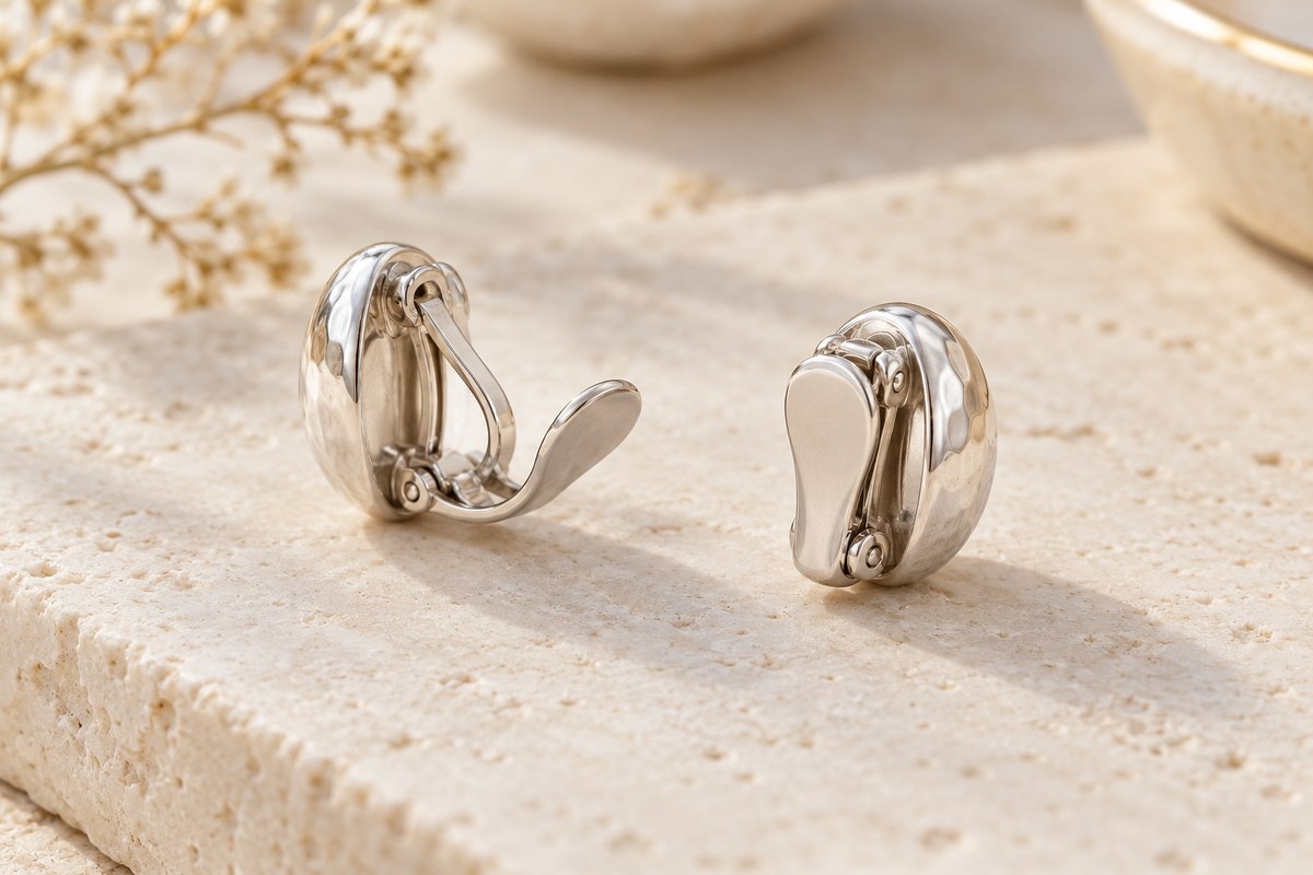 Two silver-colored clip-on earrings with open and closed paddle closures on pale stone.